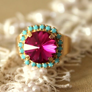 May include: A gold ring with a large, bright pink gemstone surrounded by a ring of turquoise stones.