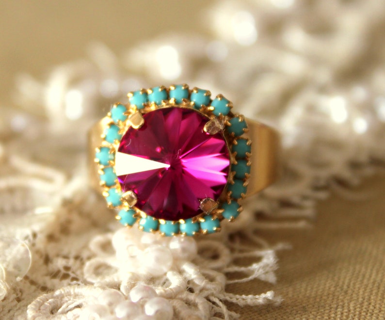 May include: A gold ring with a large, bright pink gemstone surrounded by a ring of turquoise stones.