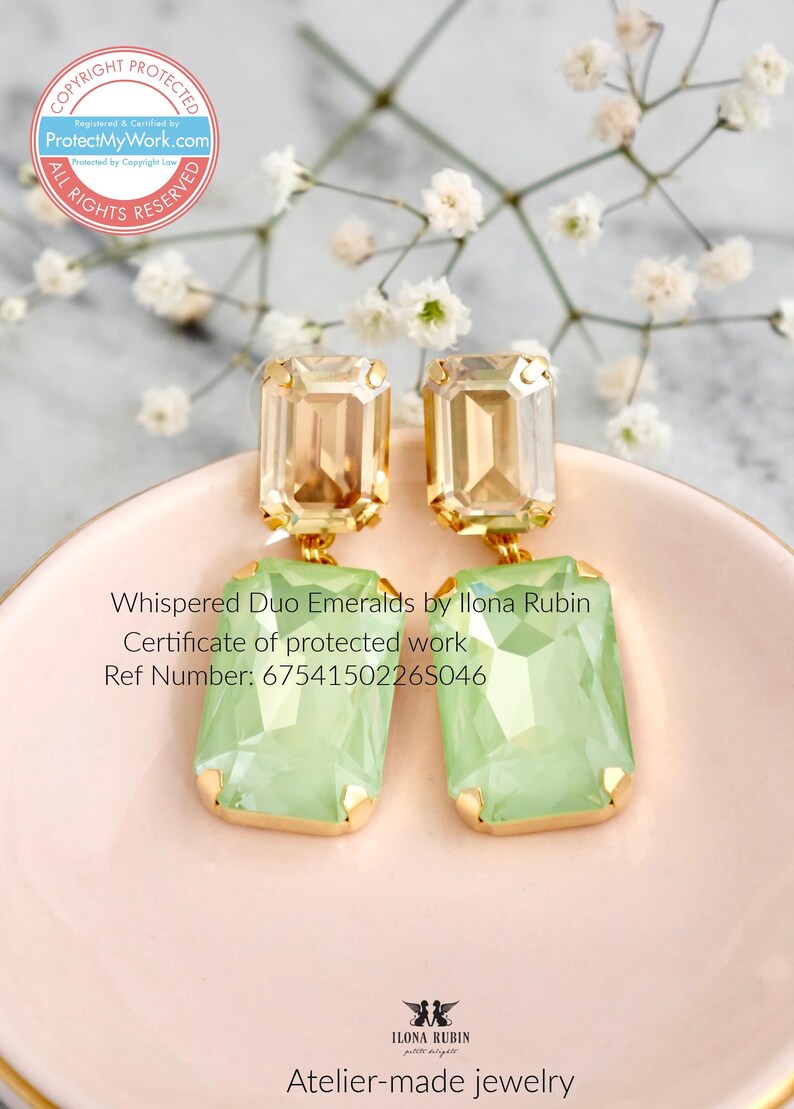 Może przedstawiać: Prostokątne kolczyki w kolorze jasnozielonym, z oprawami w kolorze złota. Kolczyki są oznaczone jako "Whispered Duo Emeralds by Ilona Rubin" i prezentowane na r&oacute;żowej powierzchni.