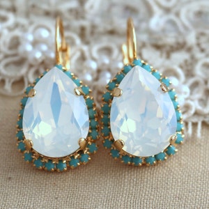 May include: A pair of gold teardrop earrings with a large white opal stone surrounded by a halo of turquoise crystals.