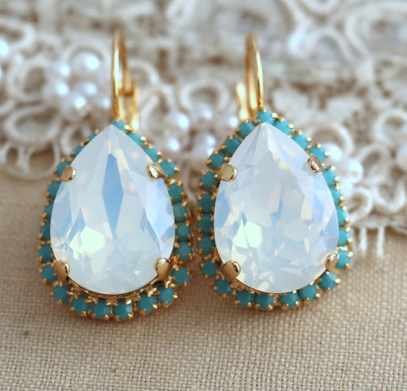 May include: A pair of gold teardrop earrings with a large white opal stone surrounded by a halo of turquoise crystals.