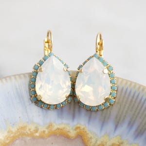 May include: A pair of gold teardrop earrings with a white opal stone and a light blue crystal halo.