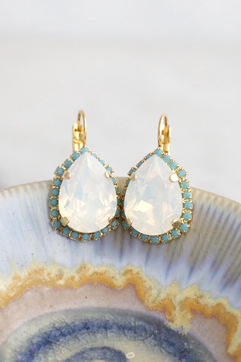 May include: A pair of gold teardrop earrings with a white opal stone and a light blue crystal halo.