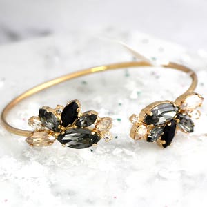 May include: A gold bangle bracelet with a cluster of black, clear, and champagne-colored rhinestones on each side.