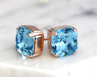 May include: A pair of rose gold stud earrings with square shaped light blue gemstones.