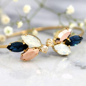May include: A gold bangle bracelet with a cluster of blue, white, and pink crystal stones in a flower shape.