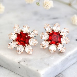 Può includere: Un paio di orecchini di cristallo rosso e trasparente con un cristallo rosso quadrato al centro di ogni orecchino. Gli orecchini sono circondati da cristalli trasparenti.