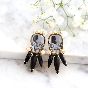 May include: A pair of gold tone earrings with black and clear crystal accents. The earrings feature a skull design with black crystal accents.
