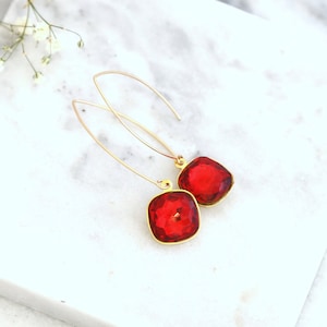 May include: A pair of gold dangle earrings with red square-shaped crystal stones.