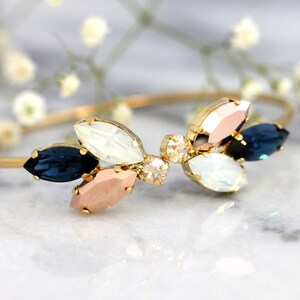 May include: A gold bangle bracelet with a cluster of blue, white, and pink crystal stones in a flower shape.