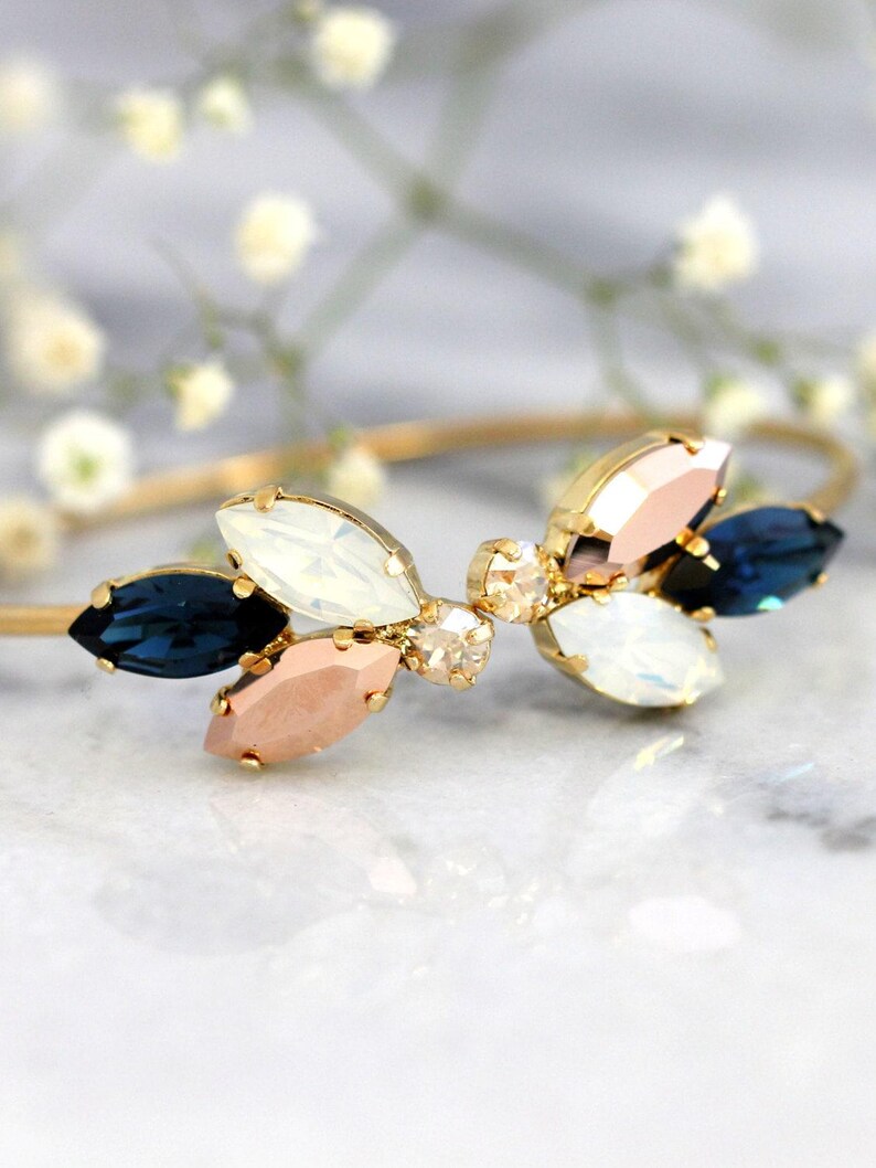 May include: A gold bangle bracelet with a cluster of blue, white, and pink crystal stones in a flower shape.