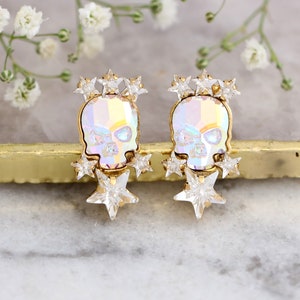 May include: A pair of gold-tone earrings featuring iridescent skull charms with clear crystal star accents.