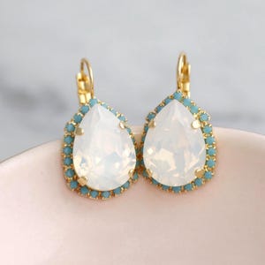 May include: A pair of gold teardrop earrings with a white opal stone and a blue crystal halo.