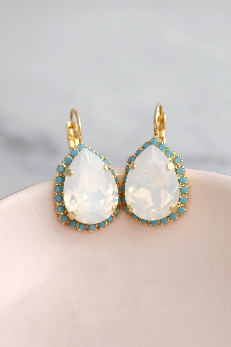 May include: A pair of gold teardrop earrings with a white opal stone and a blue crystal halo.