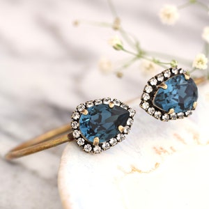 May include: A pair of gold tone cuff bracelets with teardrop shaped blue crystal stones surrounded by a halo of smaller clear crystals.