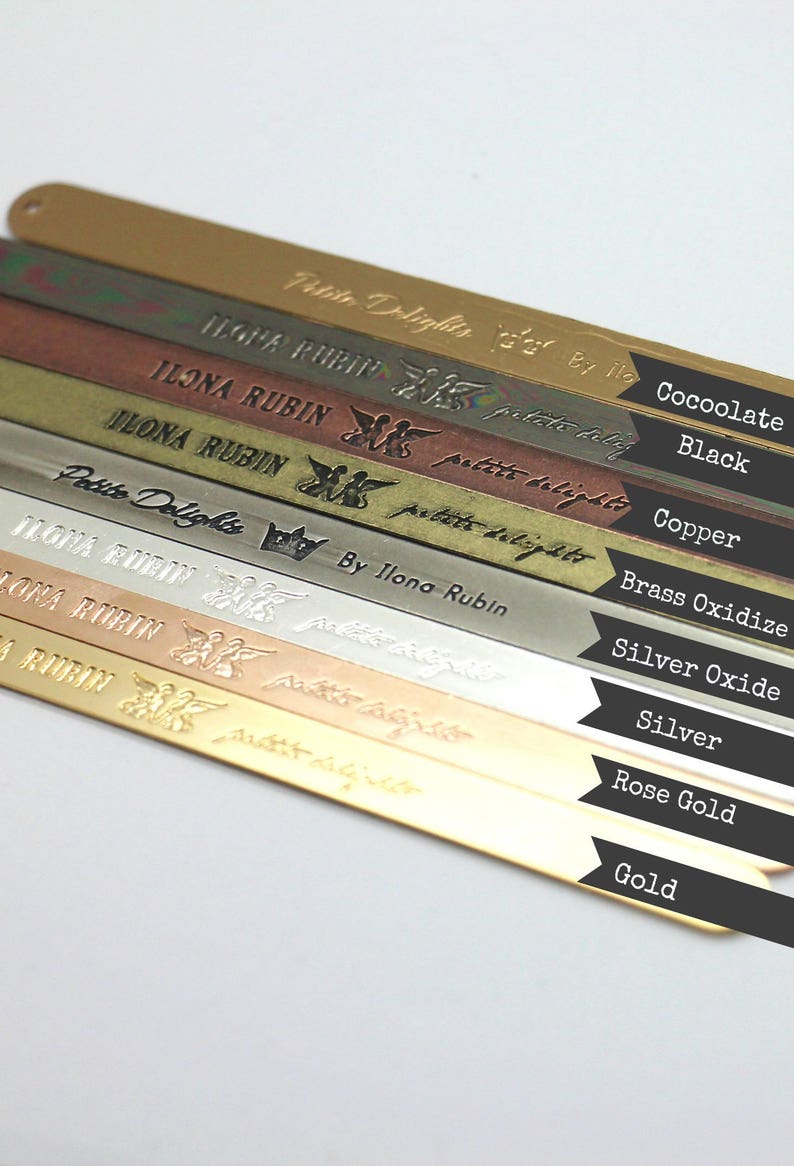 Op de afbeelding: Een close-up van tien metalen strips, elk met een andere afwerking, die de kleurvariaties van het metaal laten zien. De strips zijn gelabeld met het type metaal: Cocoolate, Zwart, Koper, Messingoxide, Zilveroxide, Zilver, Rosegoud en Goud.