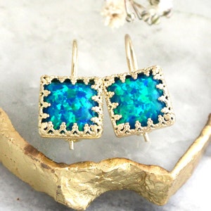 May include: A pair of square-shaped earrings featuring vibrant blue and green iridescent stones set in gold-toned metal frames with a decorative scalloped edge and attached to simple gold-toned ear wires for hanging.