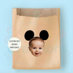 May include: A brown paper party bag featuring a Mickey Mouse face design. The design incorporates two black circles as ears and a baby's face. The bag has the text "CUSTOM FACE MICKEY PARTY BAGS" on a white circle.