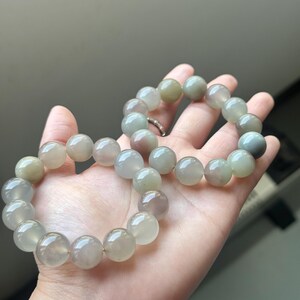 May include: A bracelet with large, spherical beads in a mix of green, grey, and purple hues. The beads are strung together, resembling a necklace. The bracelet is held in a hand.