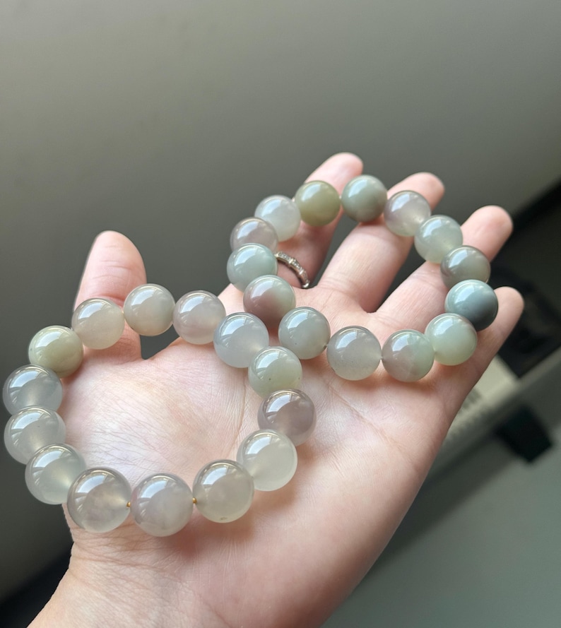 May include: A bracelet with large, spherical beads in a mix of green, grey, and purple hues. The beads are strung together, resembling a necklace. The bracelet is held in a hand.