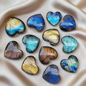 May include: A collection of heart-shaped labradorite stones. The stones display a range of colors, including blues, yellows, and browns, with iridescent flashes. The polished surfaces reflect light, creating a shimmering effect. The stones are arranged on a satin fabric.