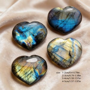 May include: Four heart-shaped labradorite stones with blue, yellow, and gray hues. The stones have a polished, glossy finish and are arranged on a soft, cream-colored fabric. The size of the stones ranges from 0.4 to 1.97 inches.