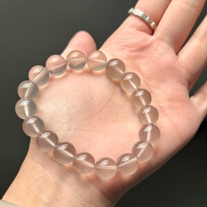 Op de afbeelding: Een armband gemaakt van doorschijnende, lichtbruine, ronde kralen. De kralen zijn aan elkaar geregen en vormen een cirkelvorm. De armband wordt op een hand getoond.