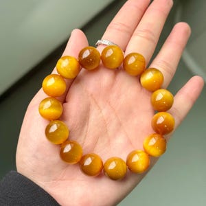 May include: A golden yellow beaded bracelet. The bracelet is made of large, round beads with a polished, reflective surface. The beads are strung together to form a circular shape. The bracelet is shown on a hand.