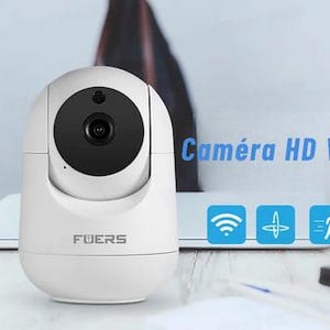 Puede incluir: Cámara inalámbrica FUERS HD WiFi blanca con lente negra. La cámara tiene un diseño redondeado y está sobre un escritorio con un portátil y una pequeña planta. El texto "Caméra HD WIFI sans fil" es azul.