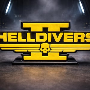 May include: A black and yellow HellDivers logo, with the word "HELLDIVERS" in yellow. The logo incorporates a skull and wing design. The logo is on a black base, set against a dark, industrial background.