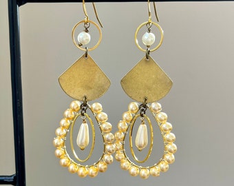 Peut inclure: Boucles d'oreilles dorées en forme de larme, avec un cercle orné d'une perle blanche, une forme géométrique dorée et un cercle de petites perles blanches.