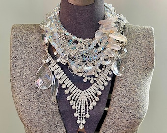 May include: A gray fabric mannequin with a layered necklace of rhinestones, crystals, and clear glass beads. The necklace is a mix of silver and gold tones.