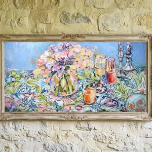 May include: An oil painting in a distressed wooden frame depicts a still life with a vase of flowers, glasses, and a patterned tablecloth. The painting hangs on a textured stone wall, with decorative plates and a sconce nearby.