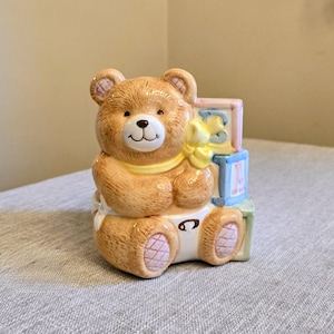 May include: A white ceramic mug with a black handle and the text "But First, Coffee" in a bold, black font. The mug is set against a blurred background, suggesting a cozy setting.