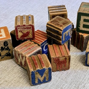 May include: A collection of weathered wooden alphabet blocks featuring various letters, numbers, and illustrations including a bird, a dog, and an umbrella. The blocks are painted in shades of red, blue, green, and orange with visible signs of wear.