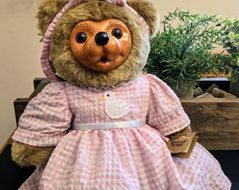 Könnte beinhalten: Ein Teddybär mit einem rosa-weiß karierten Kleid mit einem weißen Entenaufnäher. Der Bär hat ein braunes Fellgesicht und eine rosa Schleife. Das Kleid hat einen weißen Bandgürtel. Vintage Sammler Teddybär.
