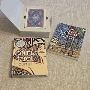 May include: A boxed deck of The Celtic Tarot cards with a blue and purple diamond pattern, a companion book titled The Celtic Tarot by Courtney Davis, and a hardcover journal titled The Celtic Tarot Journal featuring a stylized illustration of a face.