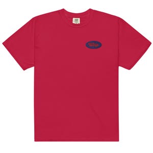 Puede incluir: Una camiseta roja con un pequeño parche ovalado azul en el pecho. El parche presenta la palabra "Welp" en una fuente estilizada. La camiseta está hecha de un material suave y tiene un cuello redondo clásico.