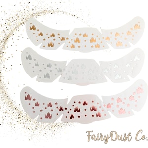 Puede incluir: Tres juegos de calcomanías blancas en forma de ala con diseños de castillo y estrella en oro, plata y oro rosa. El logotipo de FairyDust Co. está en la parte inferior derecha, con detalles de purpurina dorada.