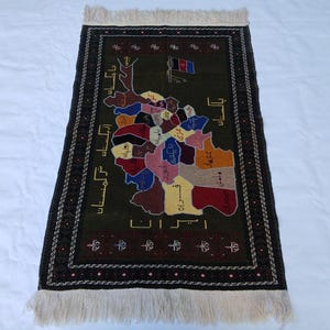 May include: A rectangular rug with a dark green background, featuring a colorful map design with various regions labeled in a foreign language. The rug has a black border with a repeating pattern and white fringe on the ends. The rug's design includes a flag.