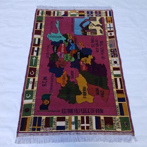 May include: A rectangular, hand-woven rug with a maroon field featuring a map of a region with country names. The rug has a border with flags and country names. The fringe is white.