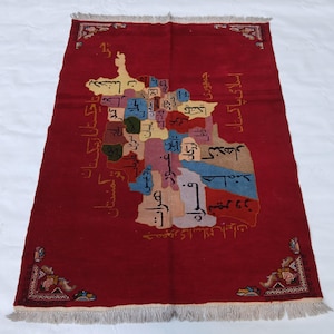 May include: A red rectangular rug with a map design. The map is multi-coloured and features text in a foreign language. The rug has decorative corner patterns and a fringed edge. The map appears to be of a Middle Eastern region.