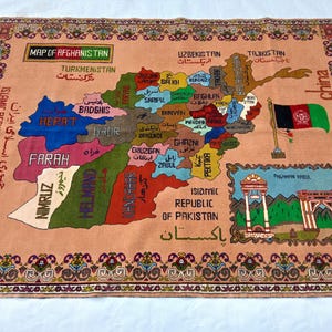 May include: A peach-coloured rug featuring a detailed map of Afghanistan, with each province colour-coded. The rug includes the country's flag, bordering countries, and text in multiple languages. The rug has a decorative border and fringe.