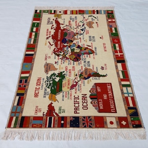 May include: A rectangular rug featuring a world map design. The map is centrally positioned, encircled by various national flags. The rug has a cream-colored backdrop with fringing along the borders. The text "World and Flags of Countries" is displayed.