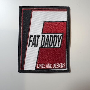 May include: Embroidered patch with the text "FAT DADDY" in white, above "LINES AND DESIGNS". The patch has a black border, a white background, and a red "F" design.
