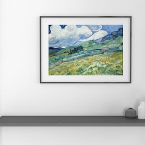 May include: Framed landscape art print featuring a vibrant depiction of rolling hills, fields, and a cloudy sky. The artwork is in a black frame and is displayed on a white wall above a gray shelf with decorative white vases and a dark gray container.