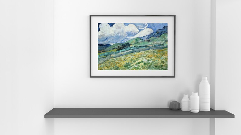 May include: Framed landscape art print featuring a vibrant depiction of rolling hills, fields, and a cloudy sky. The artwork is in a black frame and is displayed on a white wall above a gray shelf with decorative white vases and a dark gray container.