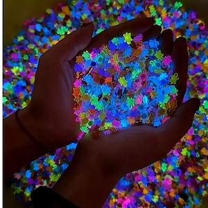 Puede incluir: Primer plano de manos sosteniendo un puñado de confeti brillante con forma de pequeñas flores. El confeti es de colores brillantes como azul, verde, naranja y morado, con un fondo de más confeti.