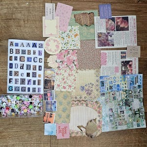 May include: A collection of craft supplies including a sheet of alphabet stickers, a rectangular container filled with small colorful floral embellishments, various patterned paper scraps, vintage-style printed cards, and a sheet of blue-toned stickers.