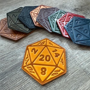 Puede incluir: Una colección de dados multicolores con textura de cuero, que incluye un dado grande de veinte caras de color naranja y varios dados cuadrados más pequeños. Los dados están grabados con números y diseños geométricos.